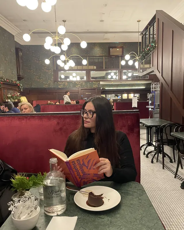 Nathália lendo um livro num café em Dublin, sentada num banco de veludo vermelho